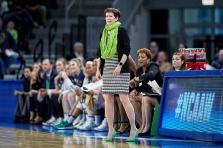 Coach Muffet McGraw in a black jacket and top at the sidelines coaching a game.